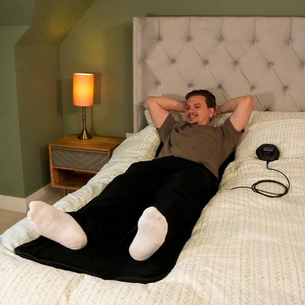 Man laying on CELLER8 full body mat in bed with CELLER8 localised applicator next to him