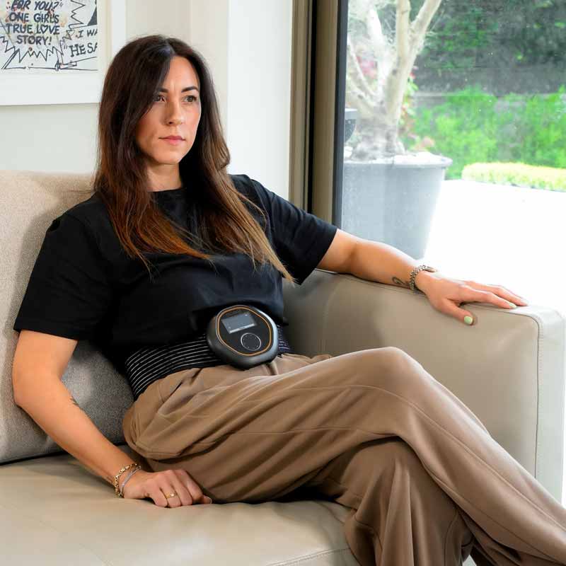 CELLER8 localised PEMF therapy device worn around women's waist while sitting on a chair