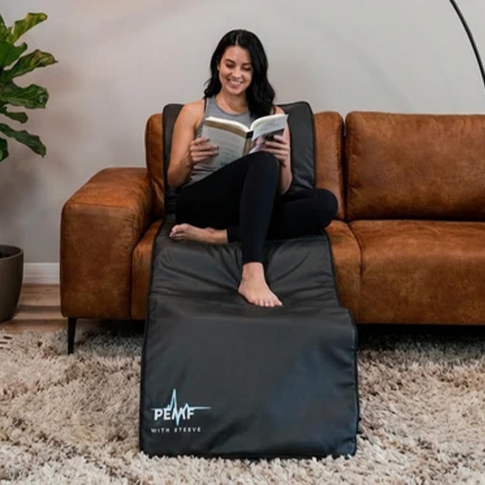 Women sat on sofa reading a book using Full Length Mat from PEMF With Steeve